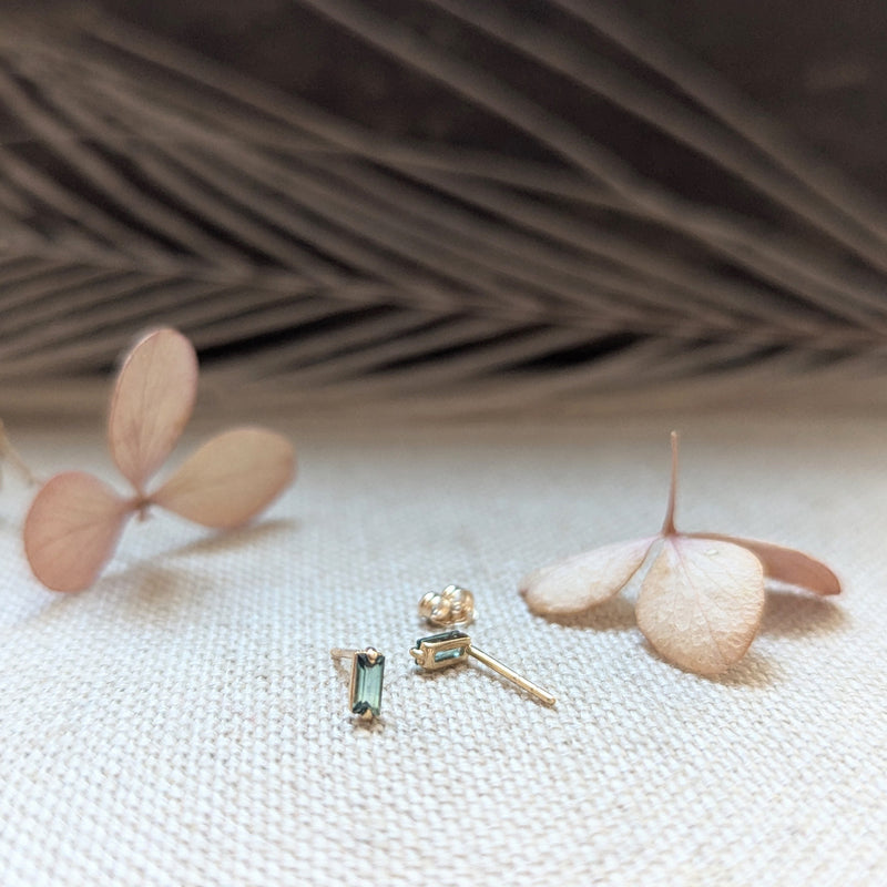 Pair of earrings with Green Tourmaline gemstones on a textured surface with dried leaves.