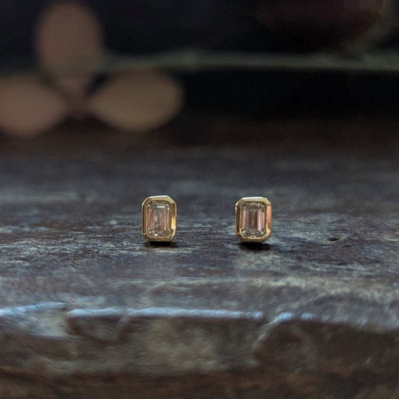 Gold stud earrings with emerald-cut dimond on a dark wood surface