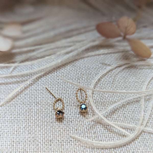 Pair of gold earrings with gemstones on a textured fabric background