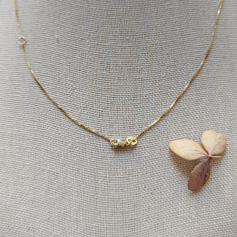 Gold necklace with a small clasp on a textured gray background 
