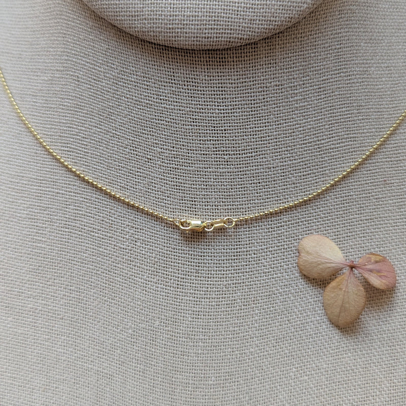 Gold necklace with clasp on a soft fabric background with a small pink flower.