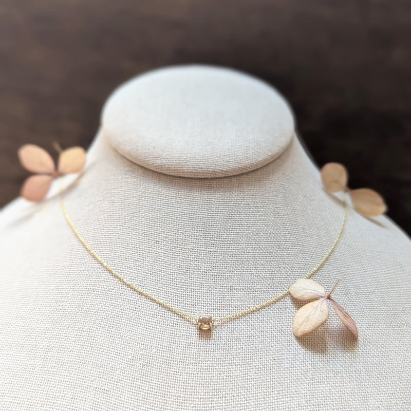 Gold necklace with dimond pendant on a mannequin bust against a dark background