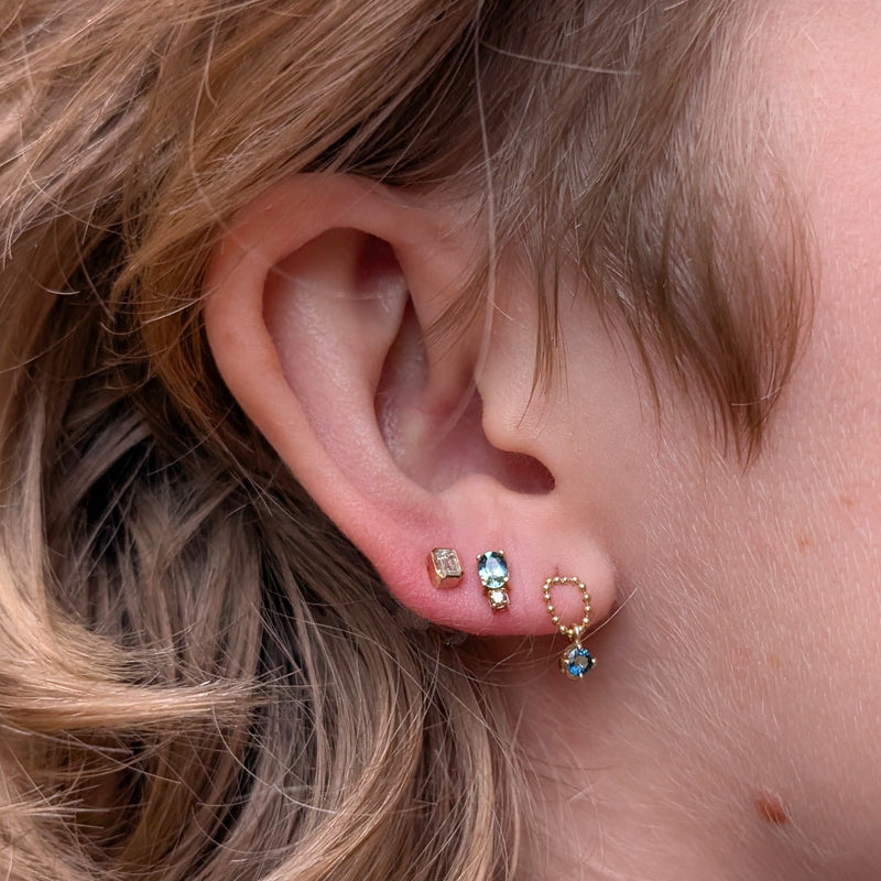 Close-up of an ear with multiple earrings on a neutral background