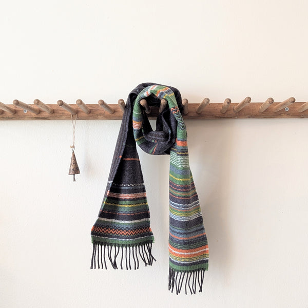 Colorful striped scarf hanging on a wooden rack against a white wall.