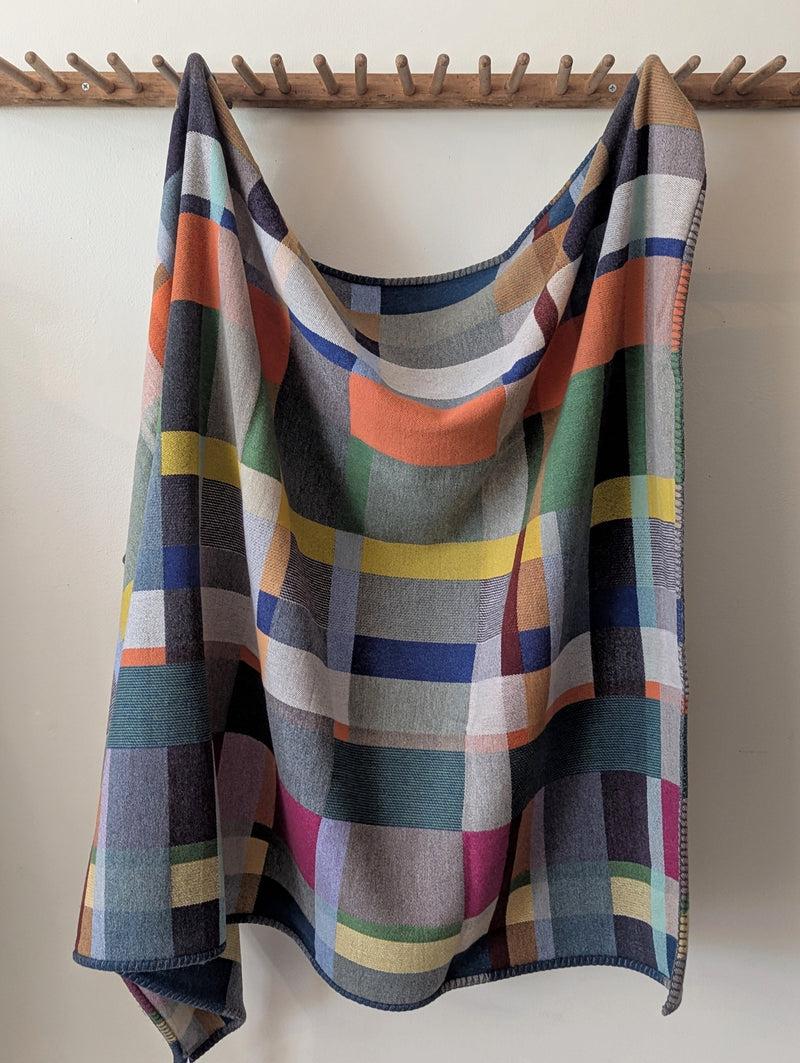 Colorful plaid blanket draped over a wooden rack against a white wall.