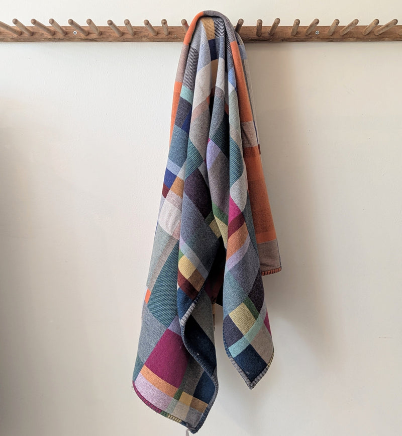Multicolored checkered towel hanging on a wooden rack against a white wall.