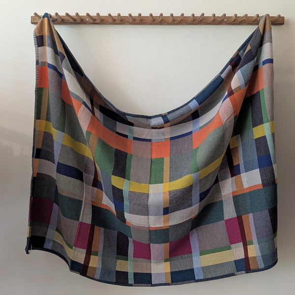 Multicolored plaid blanket draped over a wooden rod against a white wall.