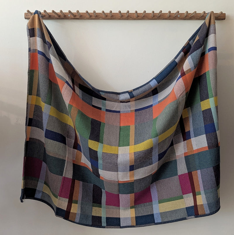 Multicolored plaid blanket draped over a wooden rod against a white wall.