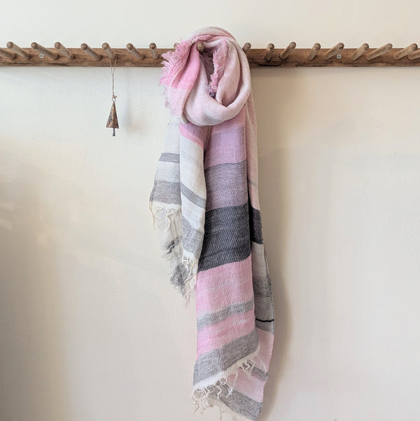 Pink and gray striped scarf hanging on a wooden rack against a white wall.