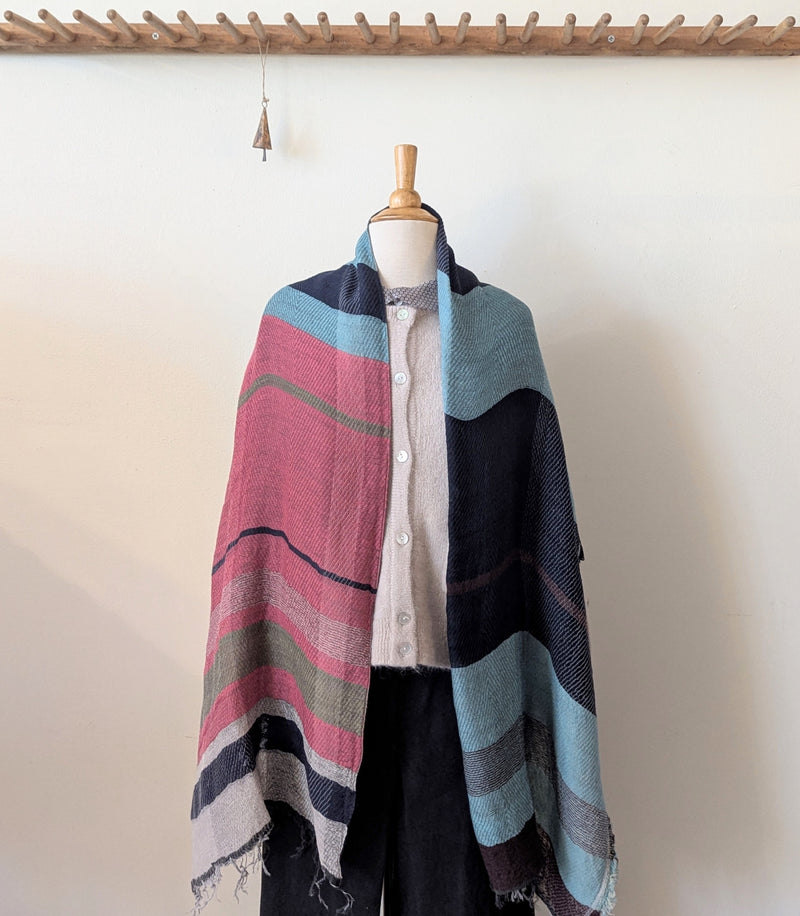 Colorful striped shawl draped over a mannequin against a white wall.