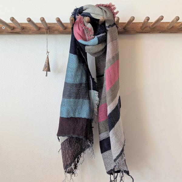 Colorful striped scarf hanging on a wooden rack against a white wall.
