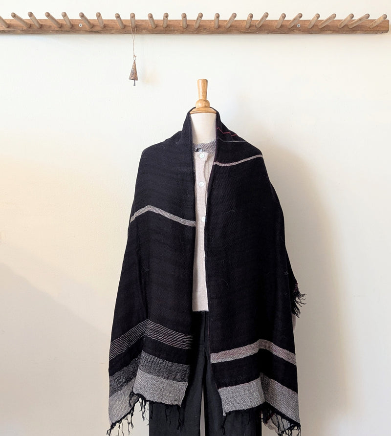Black and gray striped scarf draped over a mannequin against a white wall.