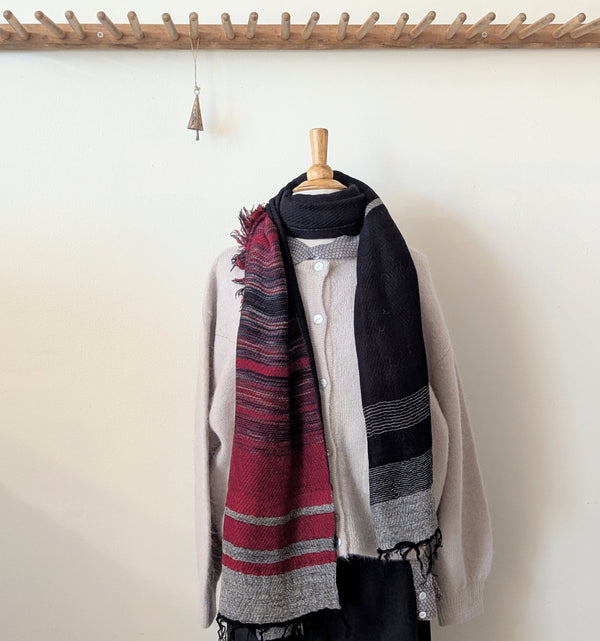 Scarf with red and black pattern draped over a mannequin against a white wall.