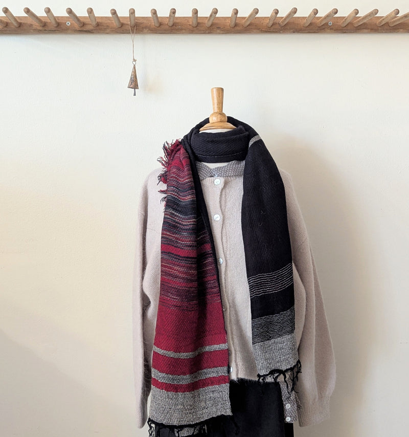 Scarf with red and black pattern draped over a mannequin against a white wall.