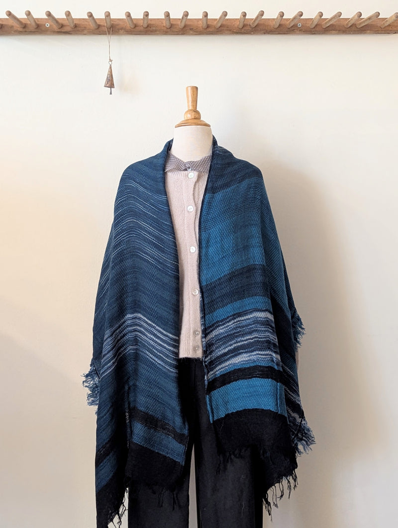 Mannequin wearing a blue and black striped poncho against a white background