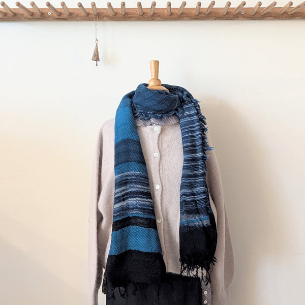 Blue striped scarf draped over a beige cardigan on a mannequin against a white wall.