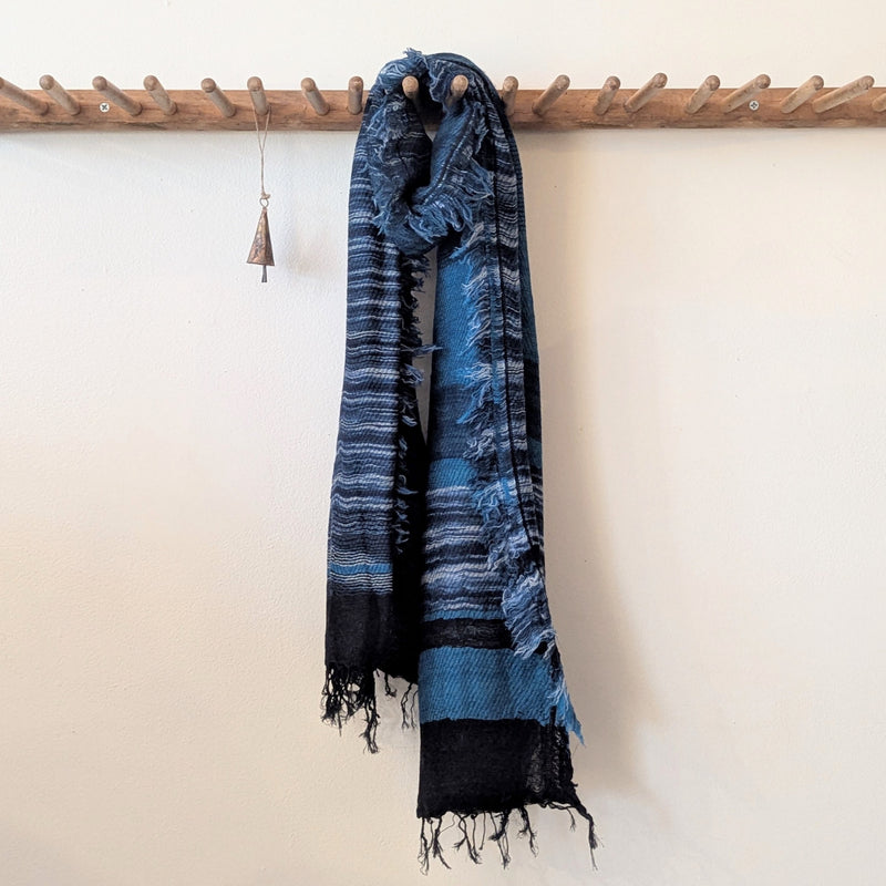Blue and black striped scarf hanging on a wooden rod against a white wall.