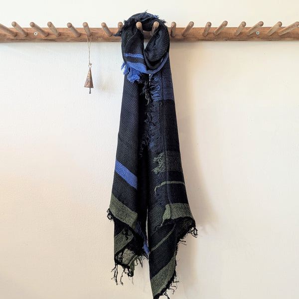 Black and blue patterned scarf hanging on a wooden rack against a white wall.