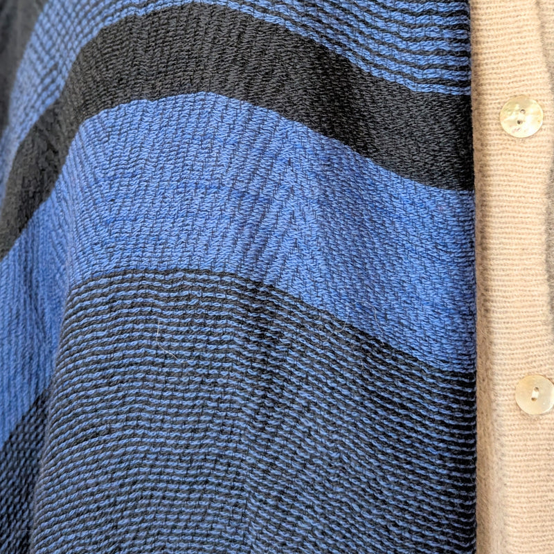Close-up of a textured fabric with blue and black stripes and a beige buttoned garment.