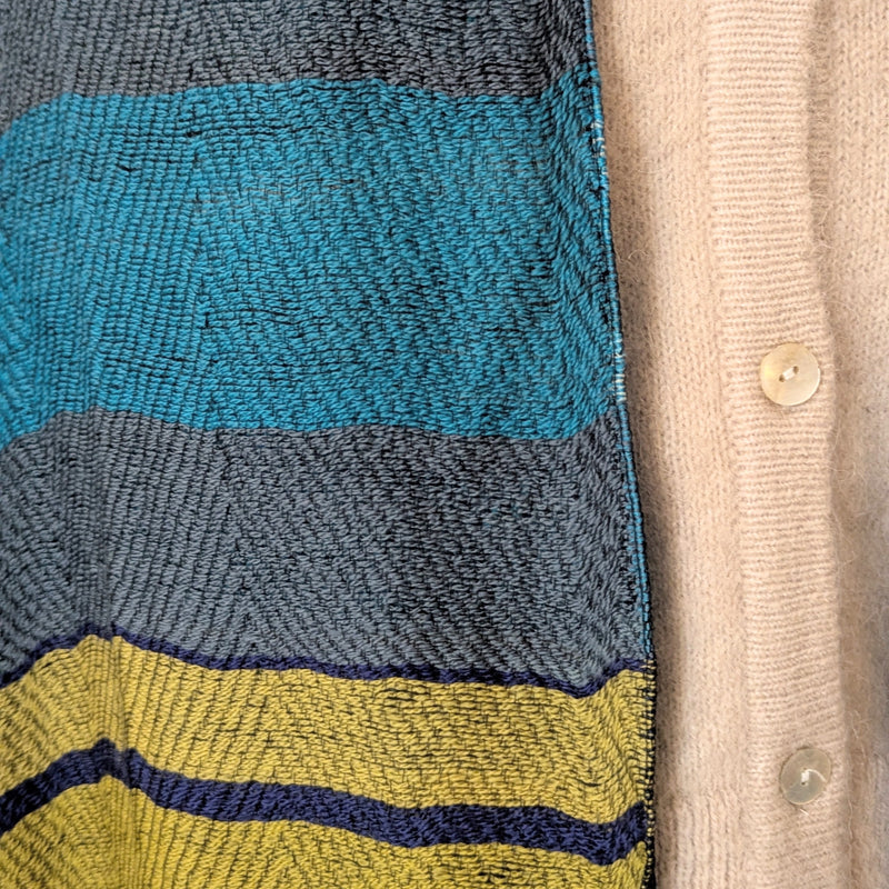 Close-up of a textured fabric with blue, gray, and yellow stripes on a beige cardigan.