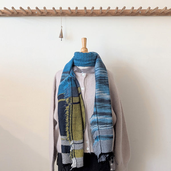 Scarf with blue and green plaid pattern draped over a mannequin against a white wall.