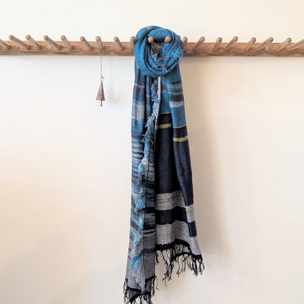 Blue and black striped scarf with tassels hanging on a wooden rack against a white wall.