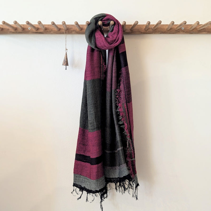 Scarf with purple and black pattern draped over a wooden rack against a white wall.