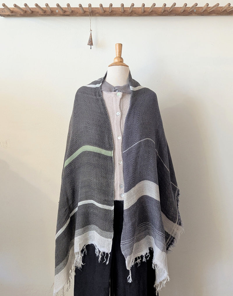 Mannequin wearing a gray striped poncho with a white shirt underneath on a plain background