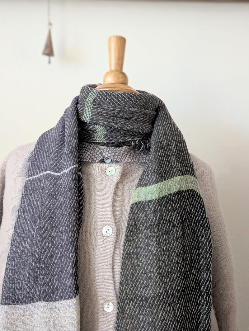 Mannequin wearing a gray and green patterned scarf with a plain background