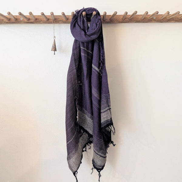 Purple scarf with black and gray patterns hanging on a wooden rack against a white wall.