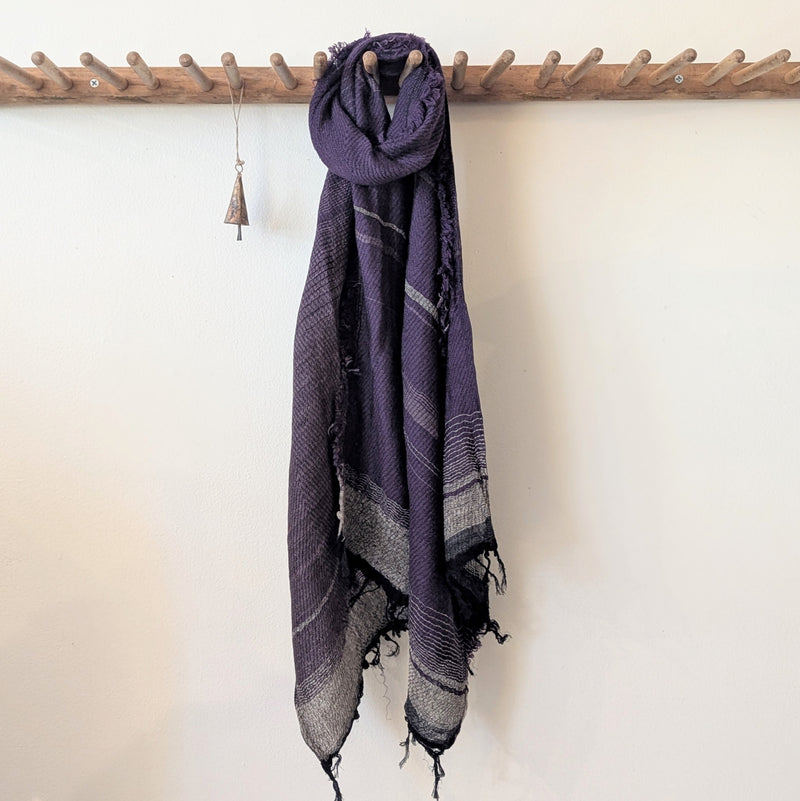 Purple scarf with black and gray patterns hanging on a wooden rack against a white wall.
