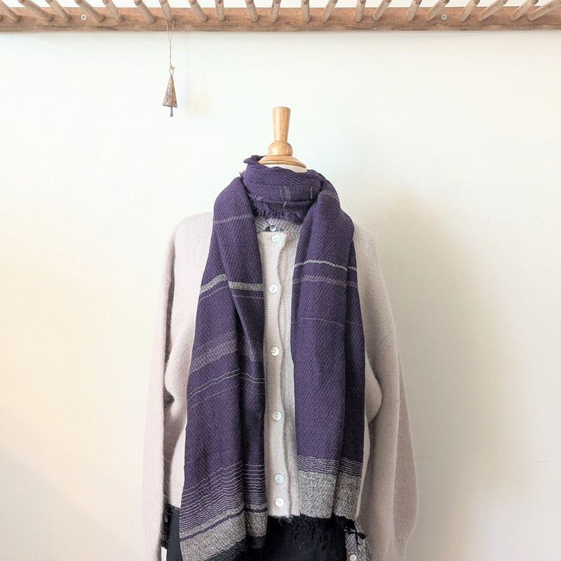 Mannequin wearing a purple plaid scarf over a light gray shirt against a white wall.