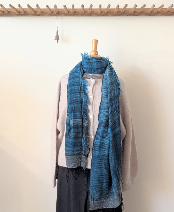 Blue stripe scarf draped over a mannequin against a white wall.