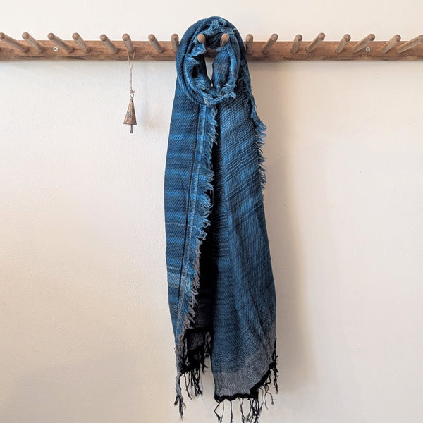 Blue stripe scarf with fringes hanging on a wooden rack against a white wall.