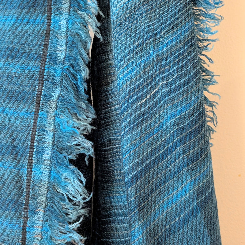 Close-up of a blue and black stripe fabric with frayed edges on a beige background