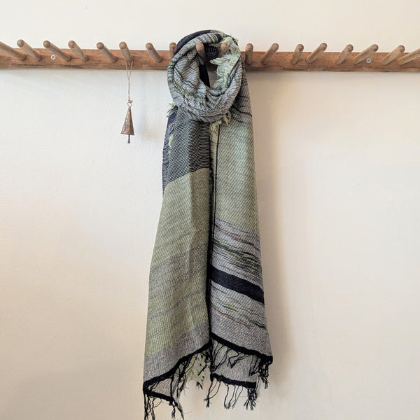 Green and black patterned scarf hanging on a wooden rack against a white wall.