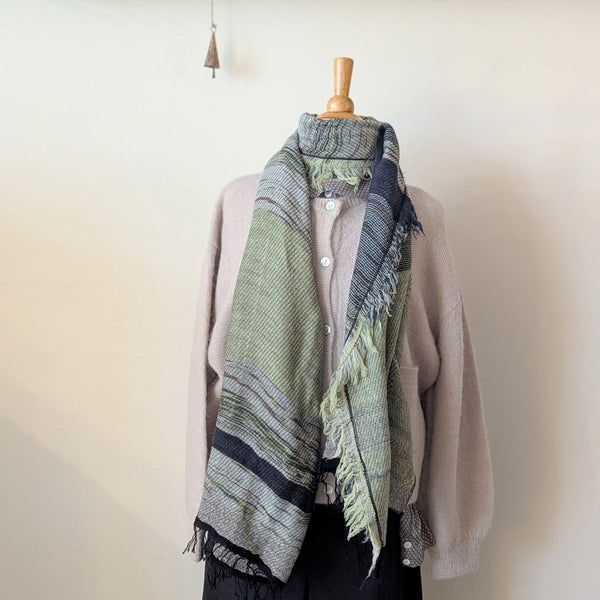 Mannequin wearing a beige cardigan with a green and blue patterned scarf on a plain background