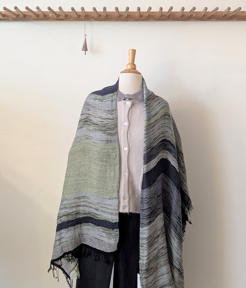 Mannequin wearing a beige cardigan with a green and blue patterned scarf on a plain background