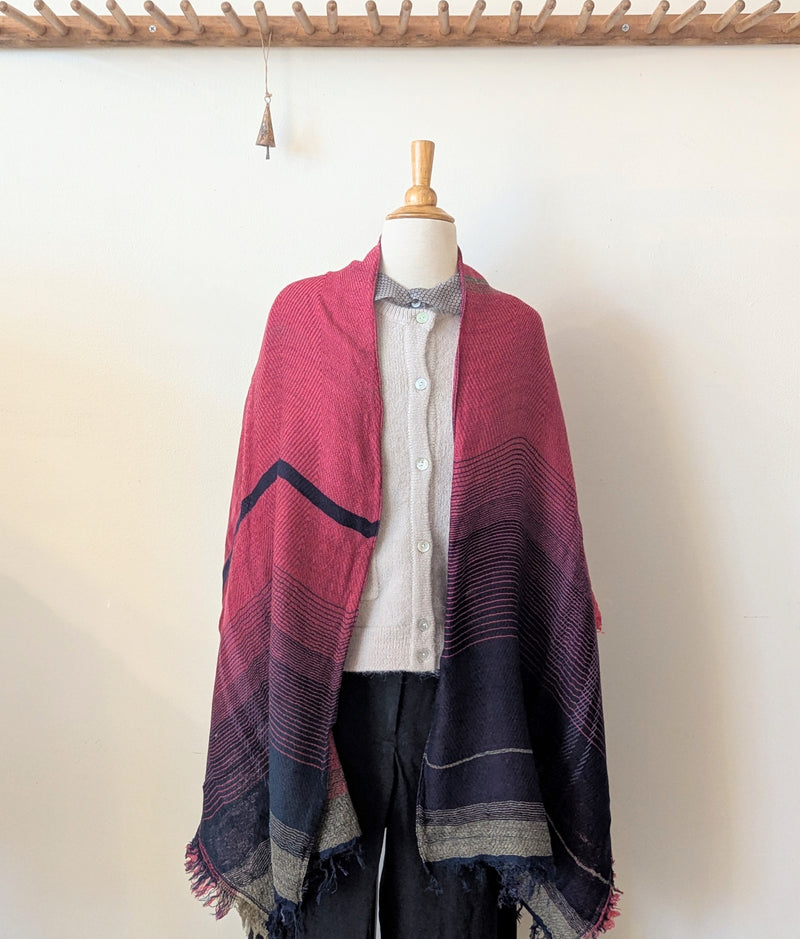 Mannequin wearing a pink and purple plaid shawl against a white wall.