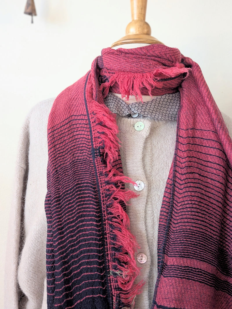 Mannequin wearing a beige sweater with a red and black striped scarf draped over it.