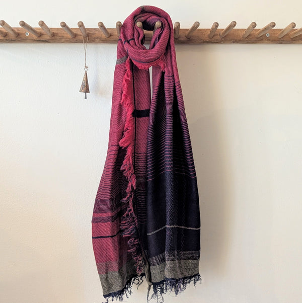 Red and black patterned scarf draped over a wooden rack against a white wall.