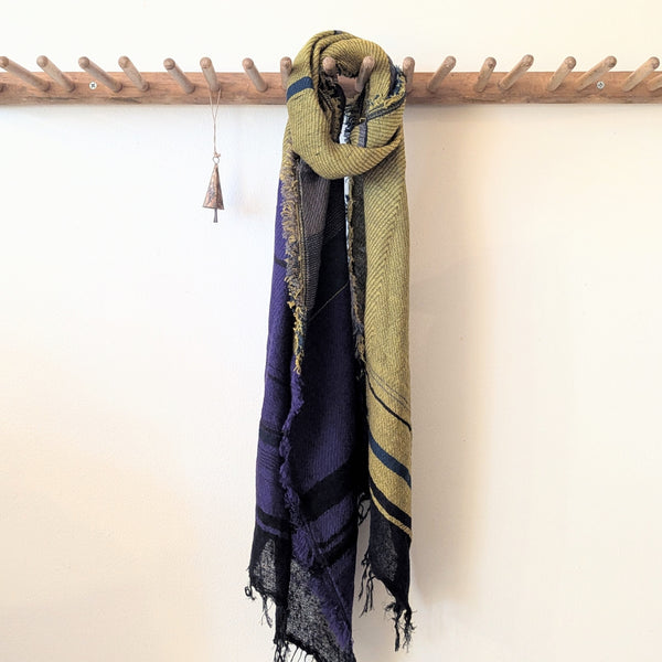 Multicolored scarf draped over a wooden coat rack against a white wall.