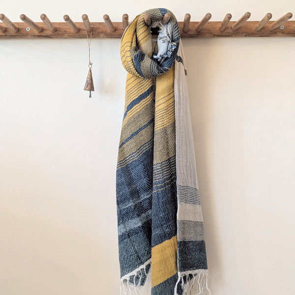 Striped scarf with blue and yellow patterns draped over a wooden coat rack against a white wall.