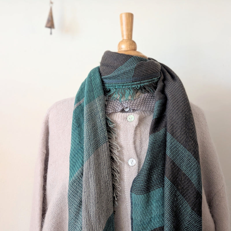 Mannequin wearing a gray sweater with a green and black patterned scarf draped over it.