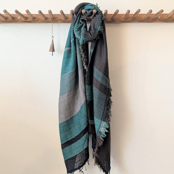 scarf with blue and gray pattern draped over a wooden rack against a white wall.