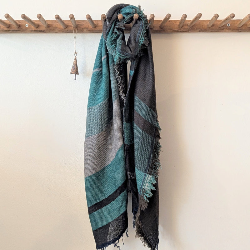 scarf with blue and gray pattern draped over a wooden rack against a white wall.