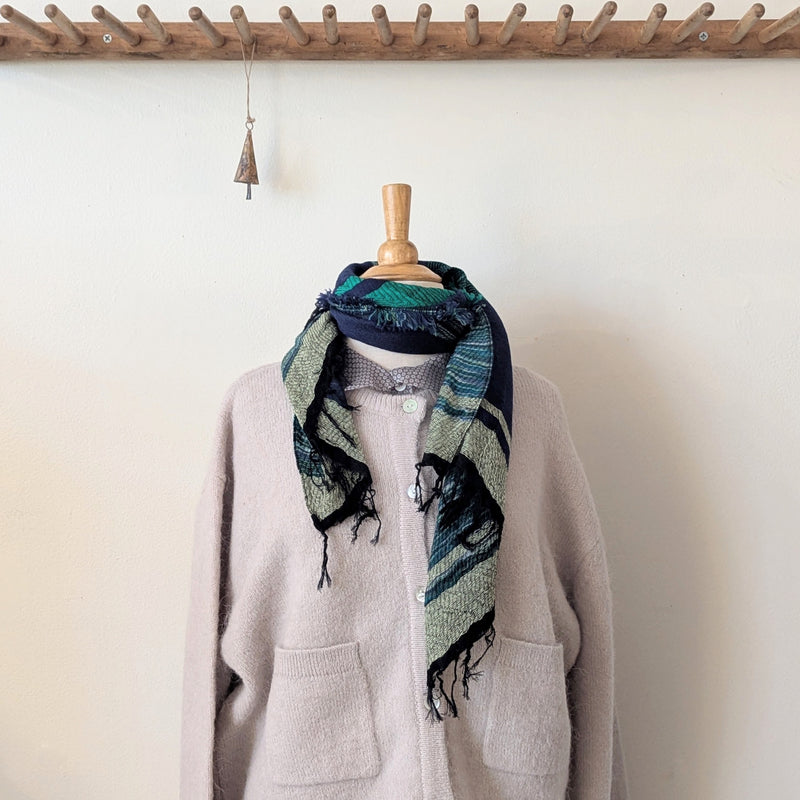Mannequin wearing a beige cardigan with a patterned scarf against a white wall.