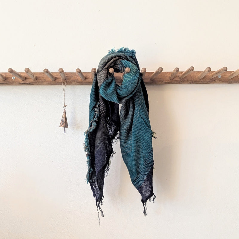 Blue and black scarf draped over a wooden coat rack against a white wall.