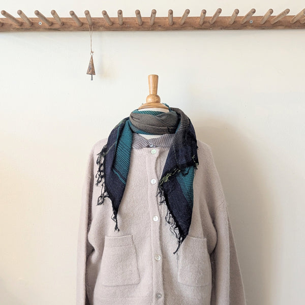 Gray cardigan with a patterned scarf draped over a wooden mannequin against a white wall.