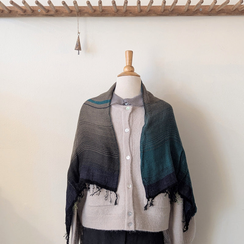 Mannequin wearing a plaid scarf over a beige shirt against a white wall.